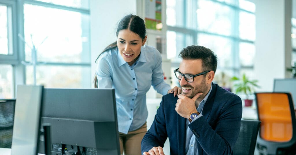 Zwei Personen beschäftigen sich mit Webdesign und Grafikdesign und erstellen gemeinsam an einem Computer in einem Büro eine Website.