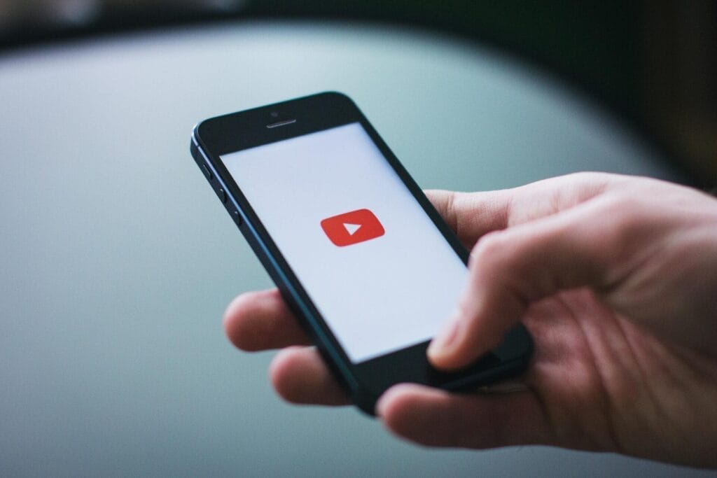 Eine Hand hält ein Smartphone, auf dem der Ladebildschirm der YouTube-App mit dem Logo der Wiedergabetaste zu sehen ist.