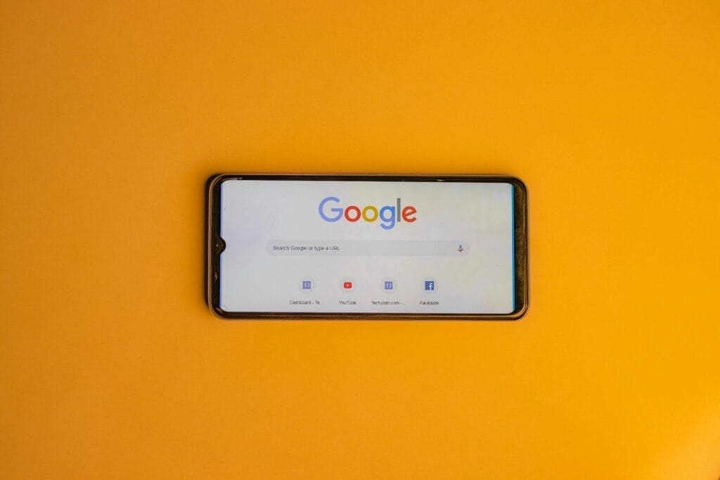 Ein Smartphone mit der geöffneten Google-Suchseite auf dem Bildschirm, platziert auf einem einfarbigen gelben Hintergrund - perfekt zur Veranschaulichung von Themen wie SEO bei Google und digitalen Strategien.