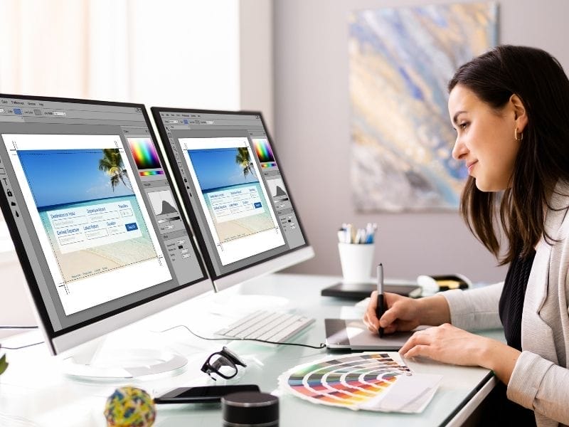 Eine Frau, die sich mit Webdesign auskennt, erstellt auf ihrem Computer mit zwei Monitoren eine Website.